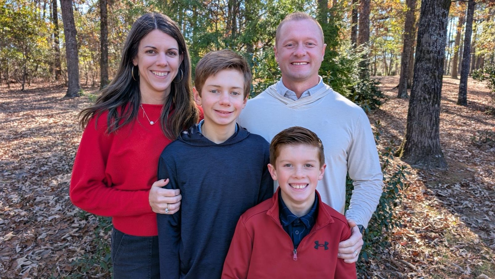 A family of four, including two boys and two adults, stand smiling in a forest.